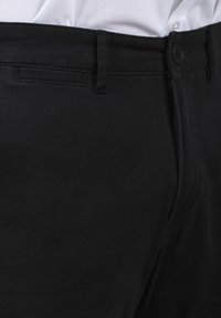 Pantalons en coton noir avec une texture lisse, présentant une taille standard, une fermeture à bouton et des poches latérales dans un design ajusté.