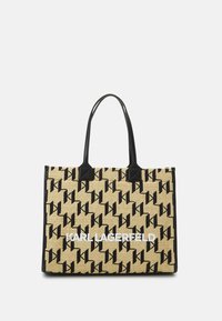 Stor tote-väska med en vävd halmtextur, svart logotypmönster, svarta läderhandtag och ett kontrasterande vitt varumärkesnamn.