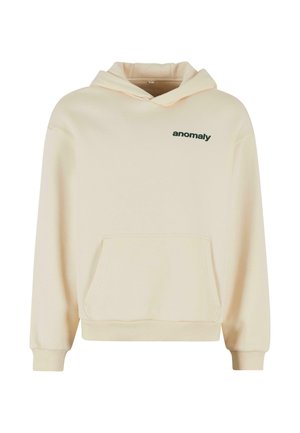 Krēmkrāsas hoodie ar priekšējo kabatu un zaļu "anomaly" tekstu uz krūtīm. Aprīkots ar kapuci ar auklām un ribotiem aprocēm. Mīksts materiāls.
