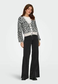 Kardigan i krämfärgad med svart leopardmönster, långa ärmar, V-hals, knäppning framtill och ribbad nederkant; kombinerad med högmidjade svarta utsvängda jeans.