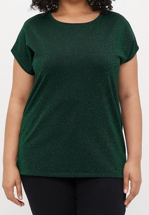 Kobieta w krótkim rękawie, ciemnozielonym błyszczącym topie i czarnych spodniach, pokazana od ramion do bioder na białym tle.