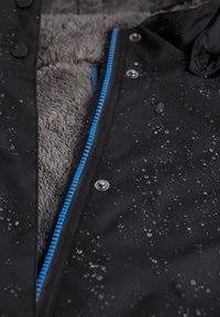 Zwarte waterdichte jas met grijze fleece voering, blauwe rits en zilveren drukknoopjes, met waterdruppels op het buitenoppervlak.