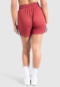 Red athletic shorts made of textured fabric with an elastic waistband. Features black and white side stripes. Worn with white socks and shoes.