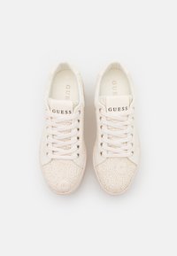 Para białych sneakersów Guess z koronkowym wzorem, z białymi sznurówkami, metalowymi oczkami i logo Guess na języku, widziana z góry.