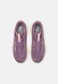 Zapatillas deportivas moradas con parte superior de tela texturizada, cierres con cordones y un acento naranja. Suela blanca acolchada, logo en la lengüeta.
