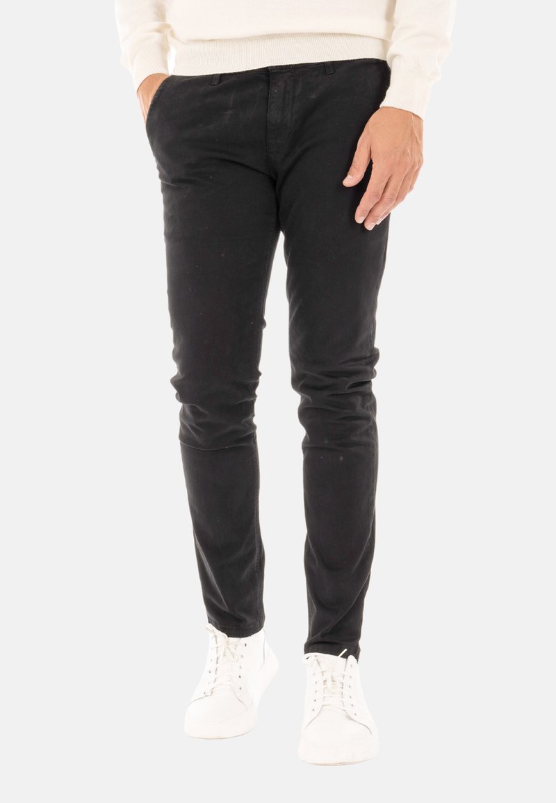 Pantaloni neri slim-fit in tessuto morbido, con vita standard e tasche. Abbinati a sneakers bianche.