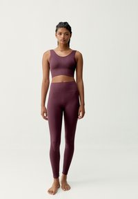 Top corto a coste color bordeaux con spalline larghe abbinato a leggings a vita alta coordinati con una texture liscia e dettagli sottili.