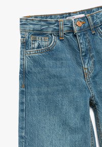 Los jeans de mezclilla de color azul claro presentan costuras naranjas en contraste, una cinturilla estándar y bolsillos delanteros con un acabado suave.