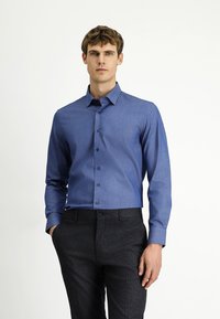 Niebieska koszula na guziki z subtelnym, teksturowanym wzorem, w połączeniu z ciemnymi, dopasowanymi spodniami. Długie rękawy i klasyczny krój kołnierzyka.