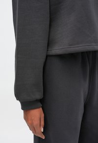 Σκούρο γκρι φούτερ και ταιριαστά joggers έχουν χαλαρή εφαρμογή, ραμμένα μανίκια και απαλή υφή, τονίζοντας την άνεση και την απλότητα.