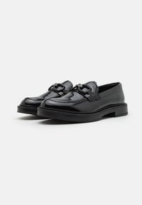 Mocassins en cuir noir avec une finition brillante, une bande décorative sur le dessus et une semelle en caoutchouc épaisse. Design classique avec des détails de couture minimaux.
