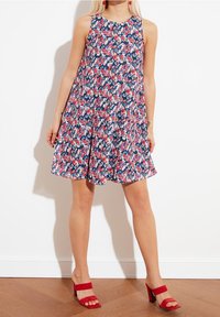 Blommig klänning i marinblått med rosa och vita mönster, ärmlös, A-linjeformad, tillverkad av lättviktsmaterial; matchad med röda klacksandaler.