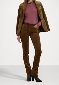 Hnědý manšestrový blejzr s vyšívaným detailem, v kombinaci s růžovým svetrem, hnědým opaskem a přiléhavými hnědými manšestrovými kalhotami. Černé boty na podpatku.