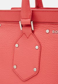 Sac en cuir texturé corail avec des accents en argent, doté d'un patch en cuir central et d'glitters métalliques, complété par des détails en couture.