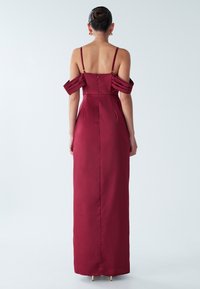 Duga haljina boje grožđa od satena s dizajnom naramenica koje se spuštaju s ramena, naboranim detaljima i uskim krojem, s neprimjetnim patentnim zatvaračem na leđima.