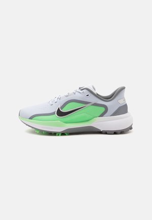 Helehall atleetlik toss neoonroheliste detailide, musta Nike'i logoga, valge tallaga ja nähtavate muruvälja naastudega, külgvaates.