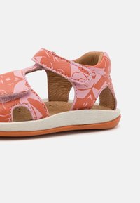 Vaaleanpunaiset nahkasandaalit leikkuukohtineen, joissa on kukkakuvio. Vaaleanruskea pohja ja teksturoitu valkoinen sisäpohja, jossa on oranssi yksityiskohta.