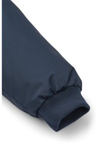 Manche bleu marine d'une veste composée d'un tissu lisse et légèrement brillant, avec un poignet élastique et une section de tissu froncé à l'épaule.