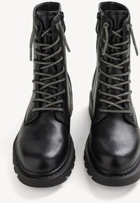 Bottes bottine en cuir noir avec bout arrondi, fermeture à lacets gris, lacets texturés et semelle épaisse en caoutchouc.
