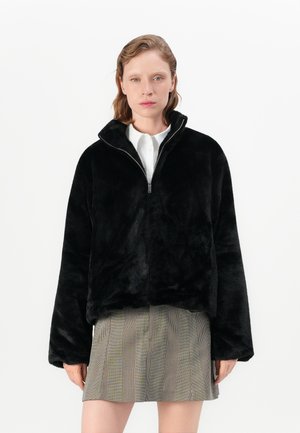 Black fleece pullover with high collar and half-zip, featuring a soft, textured finish. Paired with a checkered mini skirt.
