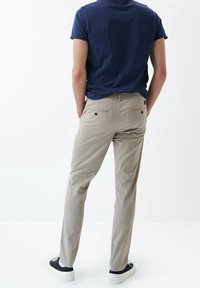 Béžové chino kalhoty s rovnoměrně střiženými nohavicemi, se zadními kapsami na knoflíková zapínání, v kombinaci s námořnicky modrým tričkem s kulatým výstřihem a černými teniskami.