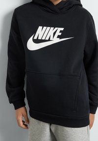 Černá mikina s kapucí vyrobená z měkké látky s velkým bílým logem Nike na přední straně. Obsahuje přední kapsu ve tvaru klokaního vaku a žebrované manžety.