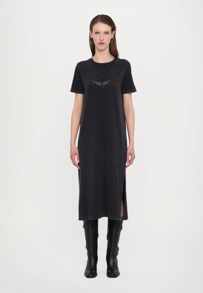 Sort T-shirt-kjole med korte ærmer, der har et perlesmykke ved halsudskæringen og sideslids, parret med høje sorte støvler.