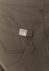 Pantalones cargo marrones con un bolsillo con cremallera, costuras en contraste y una etiqueta de logo de The North Face en la cinturilla.