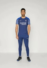 Marine atletisk tøj med en kortærmet trøje med grå accenter og "Qatar Airways" logo, parret med tætsiddende bukser og sorte støvler.