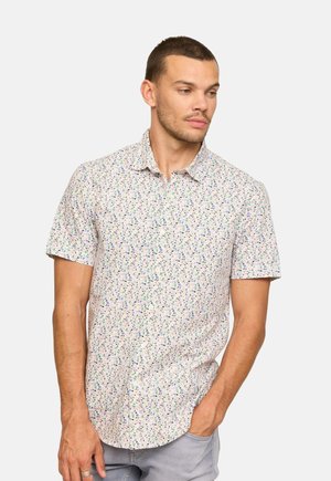 Chemise à manches courtes avec boutons, arborant un motif floral clair avec des accents verts, bleus et violets sur fond blanc.