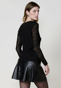 Top nero a maniche lunghe con sovrapposizione in pizzo floreale e design aderente, abbinato a una gonna a campana in pelle nera, che mette in evidenza una texture liscia.