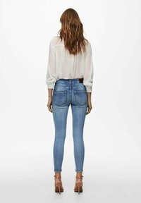 Skräddarsydda blå denimjeans med medelhög midja, bakfickor och en slät yta, ihop med en lätt genomskinlig blus med prickar.