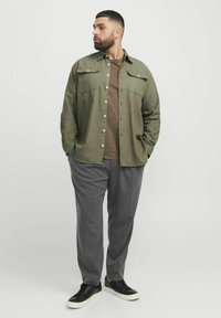 cămașă verde măsliniu cu butoni, cu două buzunare pe piept, tricou maro dedesubt, pantaloni gri cu dungi subțiri și adidași negri.