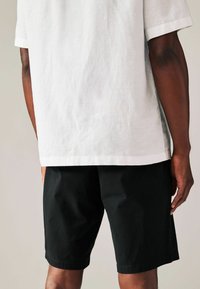 Witte linnen overhemd met korte mouwen en rechte snit, gecombineerd met zwarte katoenen shorts met een eenvoudig, gestructureerd ontwerp en geperst zoom.
