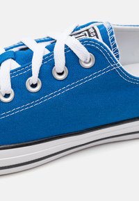 Sneaker in tela blu con lacci e occhielli bianchi, bordo della suola nera e cuciture bianche. Presenta un design classico e una superficie testurizzata.