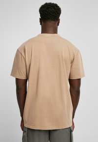 Tan bomulds T-shirt med korte ærmer, rund halsudskæring og en afslappet pasform. Stoffet ser blødt og en smule tekstureret ud.