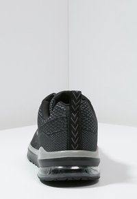 Černé sportovní tenisky s potahem z prodyšné tkaniny, s poutkem se vzorem chevron, a viditelnou vzduchovou mezipodešví, zobrazené zezadu.