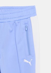 Ανοιχτό μπλε αθλητικό παντελόνι με λευκή ρίγα στο πλάι, ελαστική μέση, τσέπη με φερμουάρ και λευκό λογότυπο Puma κοντά στην τσέπη.