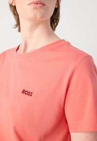 Koralo spalvos apvalios kaklo marškinėliai, pagaminti iš minkštos medvilnės, su trumpomis rankovėmis ir mažuoju šilkografijos "BOSS" logotipu kairiajame krūtinės šone.