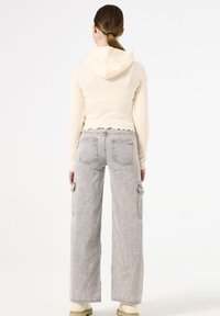 Sudadera corta de crema con mangas largas, dobladillo festoneado y capucha, combinada con pantalones cargo de pierna ancha en gris claro con múltiples bolsillos.
