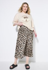 Beige graphic t-shirt met palmbomenontwerp, gecombineerd met wijduitlopende broek met leopardprint. Zwarte slide sandalen maken de outfit compleet.