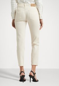 Ivory enkel-lange jeans met een aansluitend ontwerp, subtiele achterzakken en een leren label op de tailleband. Gecombineerd met zwarte hoge hakken sandalen.