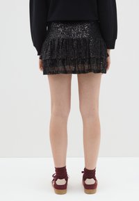 Minigonna nera con paillettes, con strati di volant, superficie testurizzata e vita aderente, abbinata a scarpe e calze bordeaux.