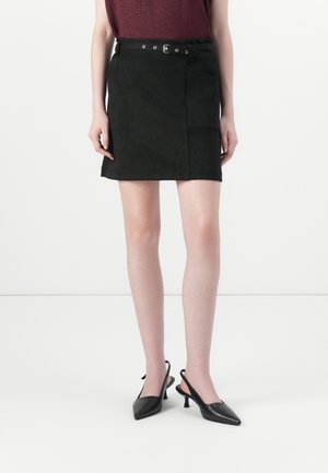 Svart semsket mini skjørt med sidelommer, belte i midjen og glatt tekstur. Kombinert med spisse svarte slingback hæler.