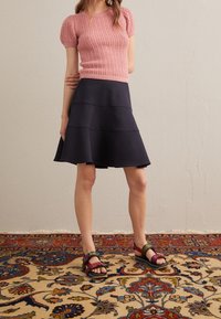 Top de punto corto en rosa claro, falda acampanada en azul marino con diseño en capas y sandalias de tiras multicolores en rojo, verde y negro.