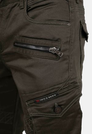 Dark green cargo pants featuring multiple pockets, textured fabric, zippered pocket detail, and contrasting stitching. Brand logo visible.