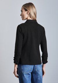 Zwarte lange mouw top met kraag, gemaakt van een textuur gebreid materiaal. Gepaard met blauwe jeans die accentstuds aan één kant hebben.