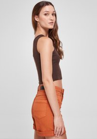 Un crop top sans manches marron associé à un short en denim orange avec des ourlets retroussés, cinq poches et une étiquette en cuir noir sur la ceinture.