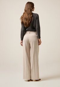 Pantalones de pana anchos de color beige con costuras verticales, bolsillos y una cinturilla ajustada, combinados con un suéter de punto gris oscuro.
