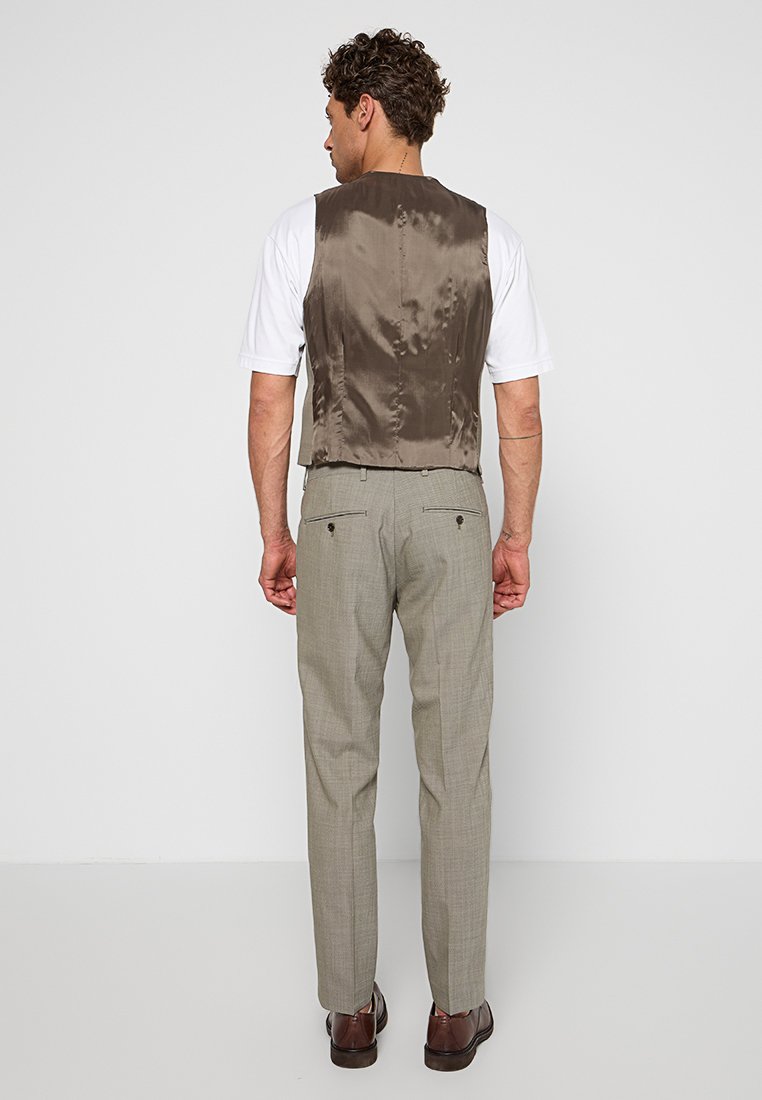 Gilet satiné marron sur une chemise blanche, avec un pantalon à carreaux gris clair et des chaussures marron, vue de l'arrière. Coutures et boutons enfermés visibles.